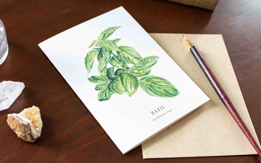 Note card with basil illustration on a wooden desk with a pen and crystal.