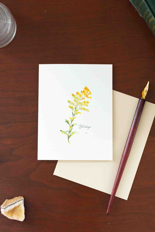 Greeting card with yellow Goldenrod illustration on a wooden surface with a pen and rock.