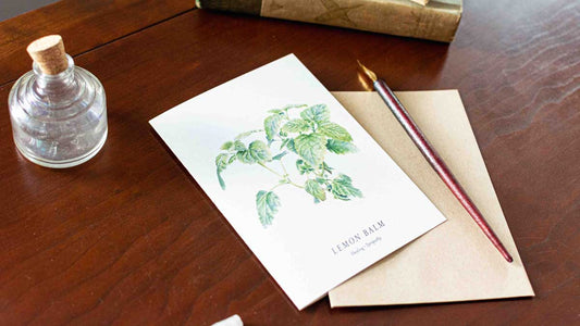 Card with lemon balm illustration on a wooden desk with a bottle and pen.