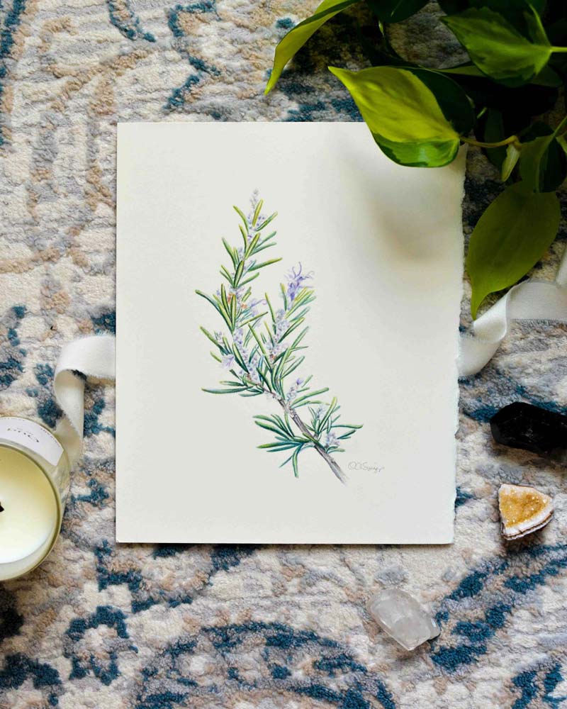 An original watercolor painting of a rosemary sprig with green needles and small purple flowers, displayed on a patterned rug with a candle, green leaves, and crystals.