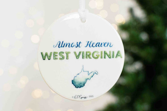 Round ornament with 'Almost Heaven West Virginia' text and outline of West Virginia on a blurred Christmas tree background.