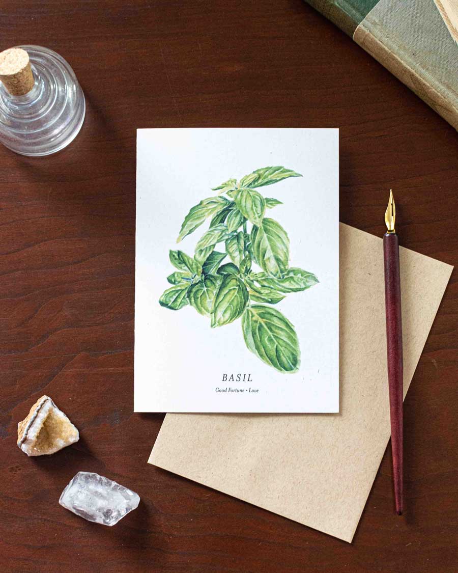 Card with basil illustration on a wooden desk with a pen and crystals.