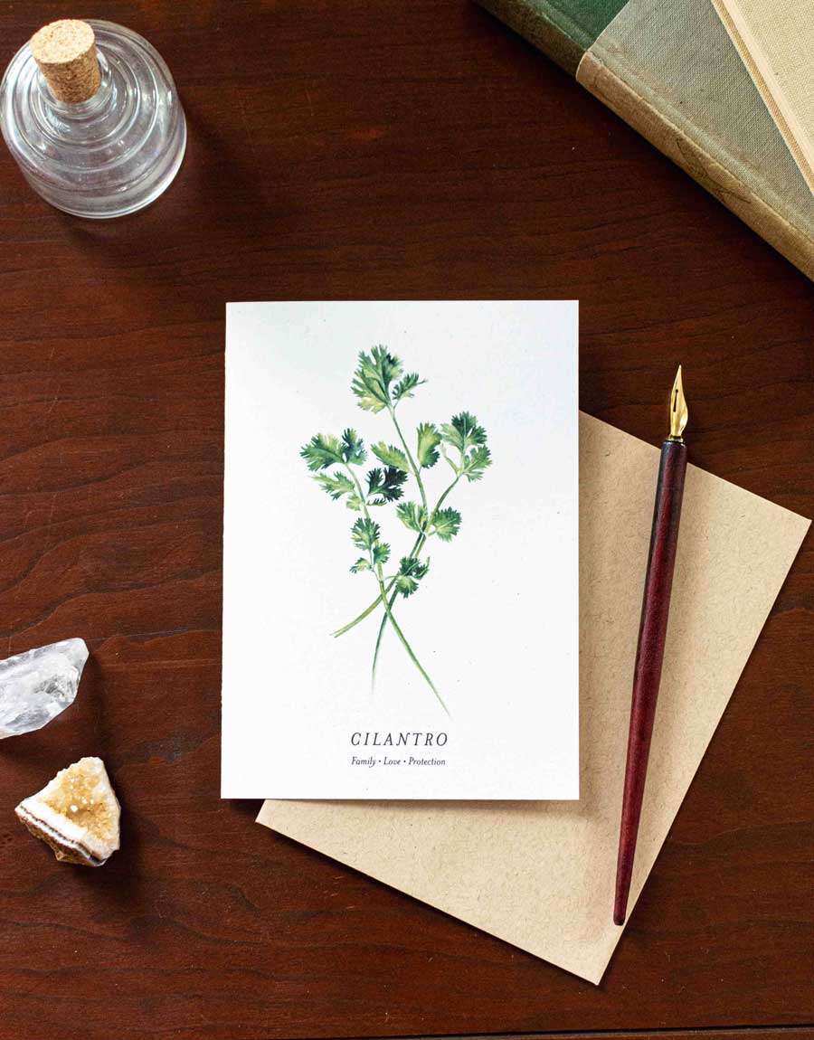 Greeting card with cilantro illustration on a wooden desk with a pen and crystal.