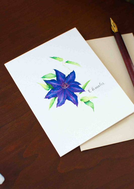 Greeting card with a deep purple Clematis flower illustration on a wooden surface