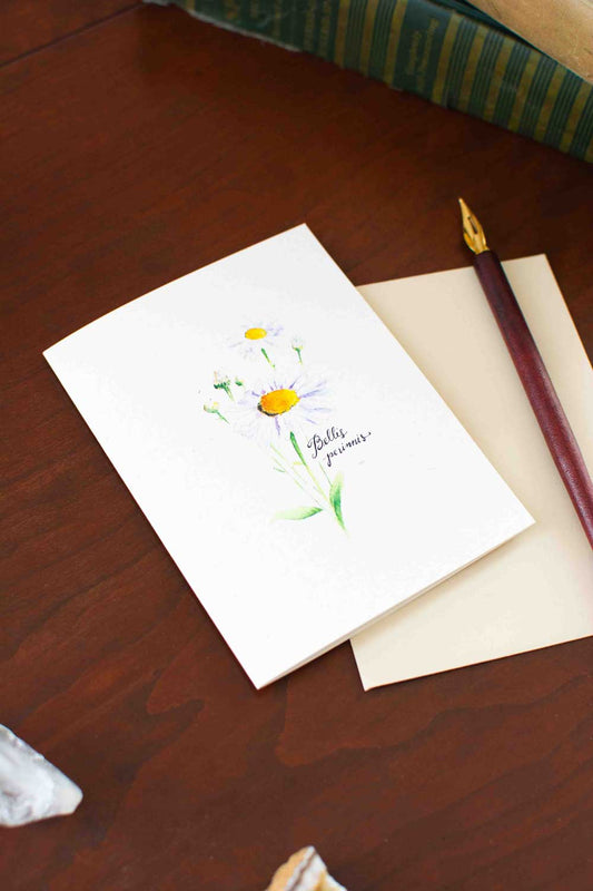 Greeting card with floral Daisy design and pen on wooden surface