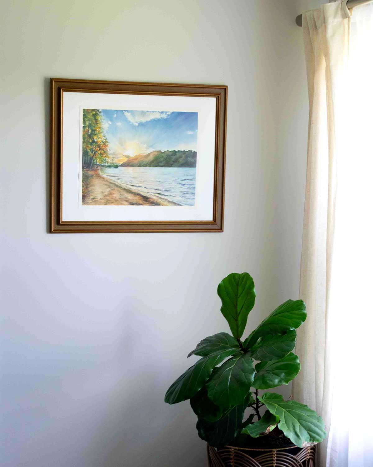Framed artwork of Cheat Lake Beach on a wall with a plant below.