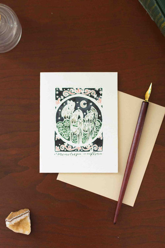 Greeting card with decorative Ghost Flower design on a wooden surface with a pen and envelope.
