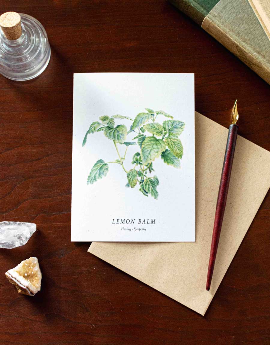 Card with lemon balm illustration on a wooden desk with a pen and crystals.