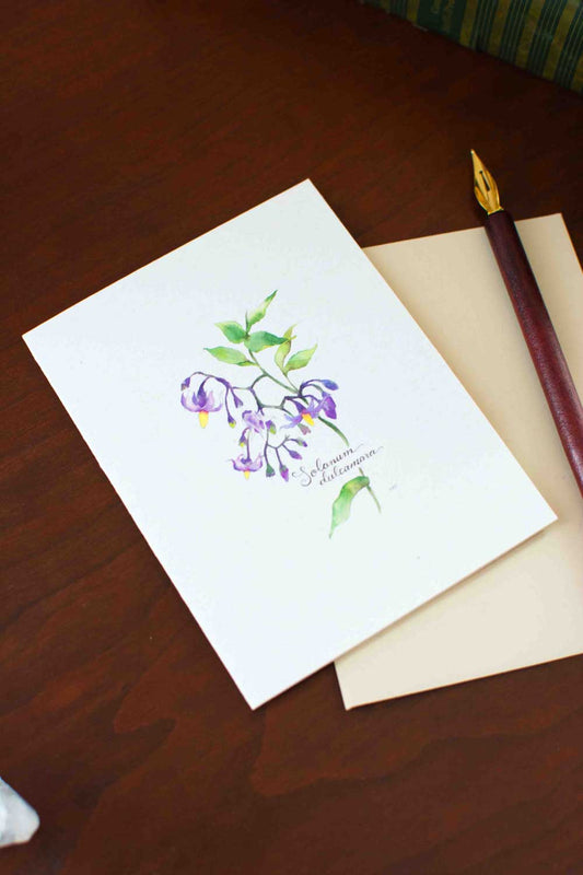 Greeting card with floral Nightshade design on a wooden surface with a pen.