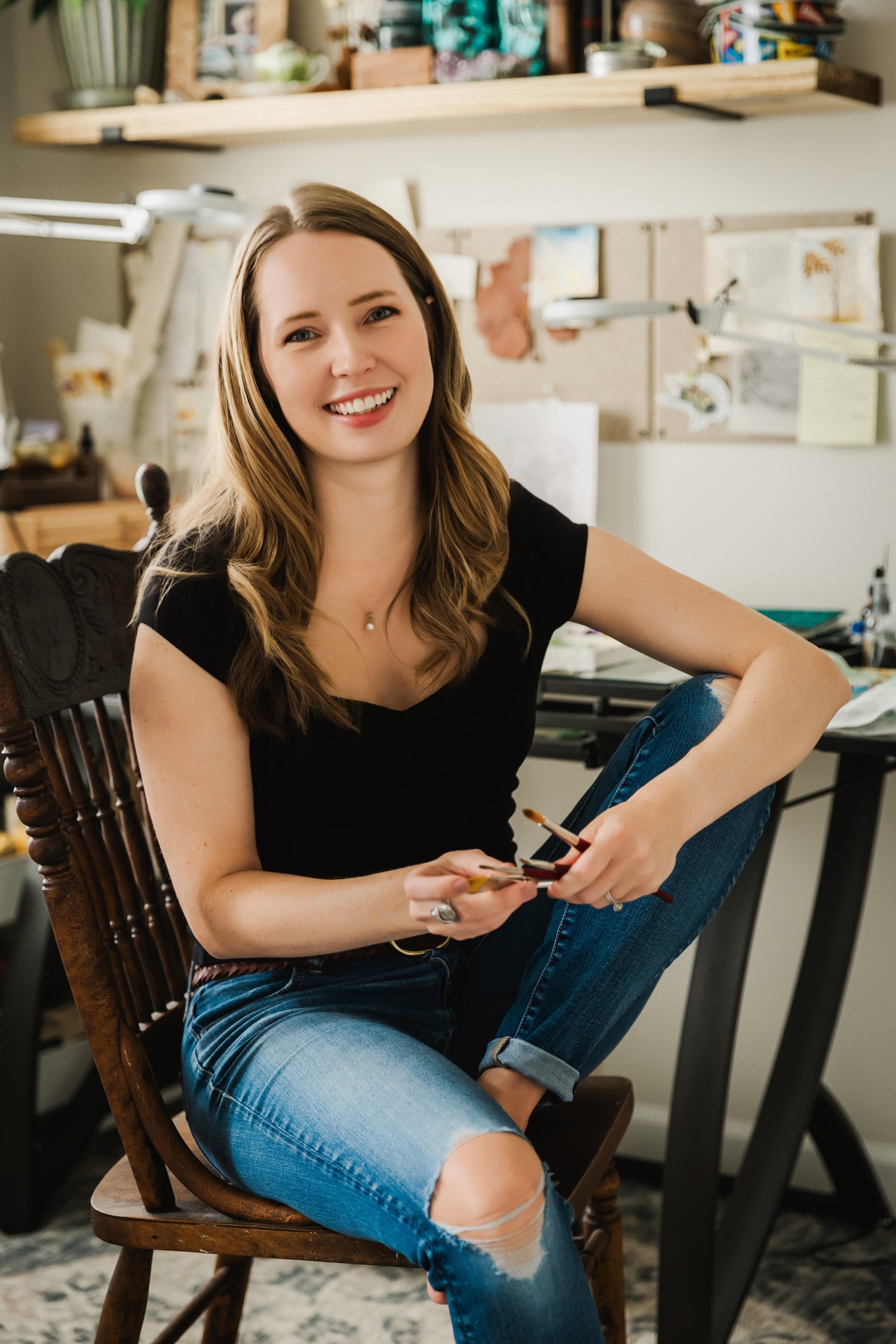 Octavia Spriggs holding paintbrushes at her painting desk