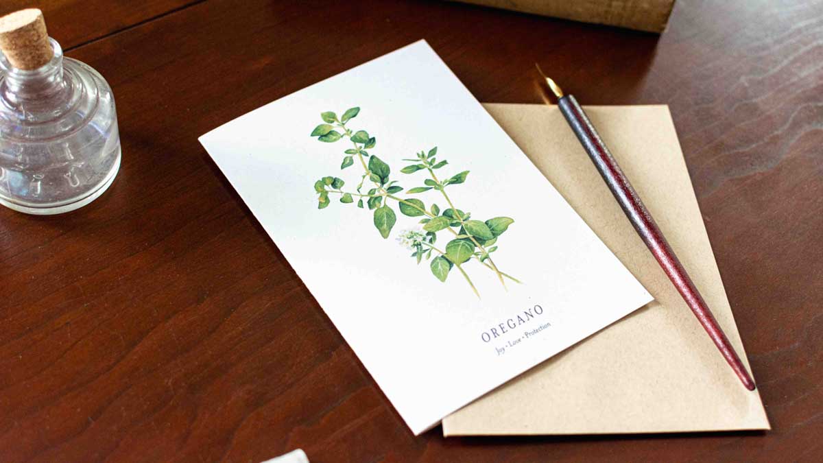 Note card with oregano illustration on a wooden desk with a pen and envelope.