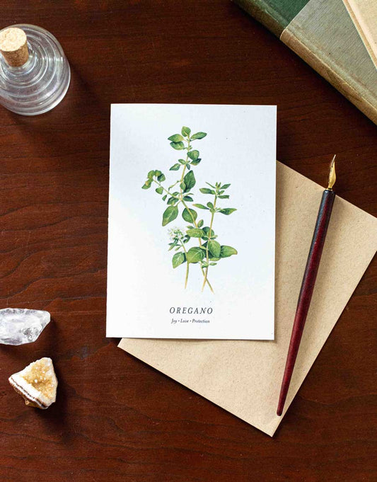 Card with oregano plant illustration on a wooden desk with a pen and crystals.