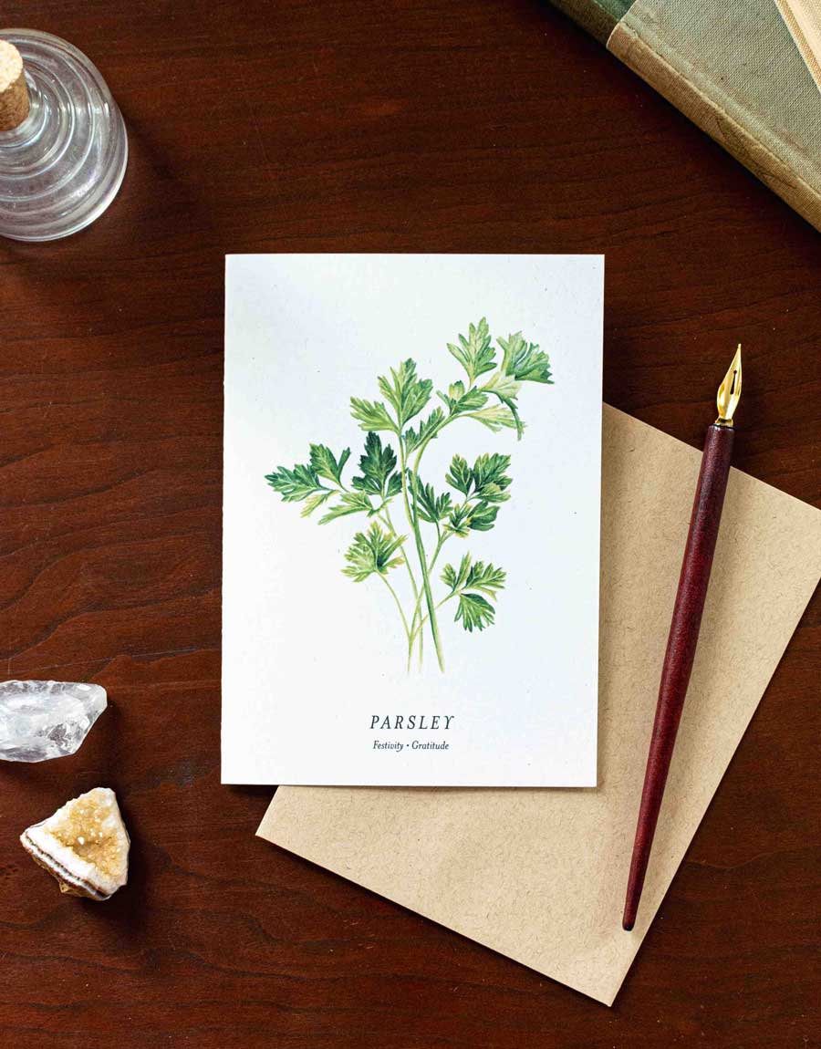 Card with parsley illustration on a wooden desk with a pen and crystals.