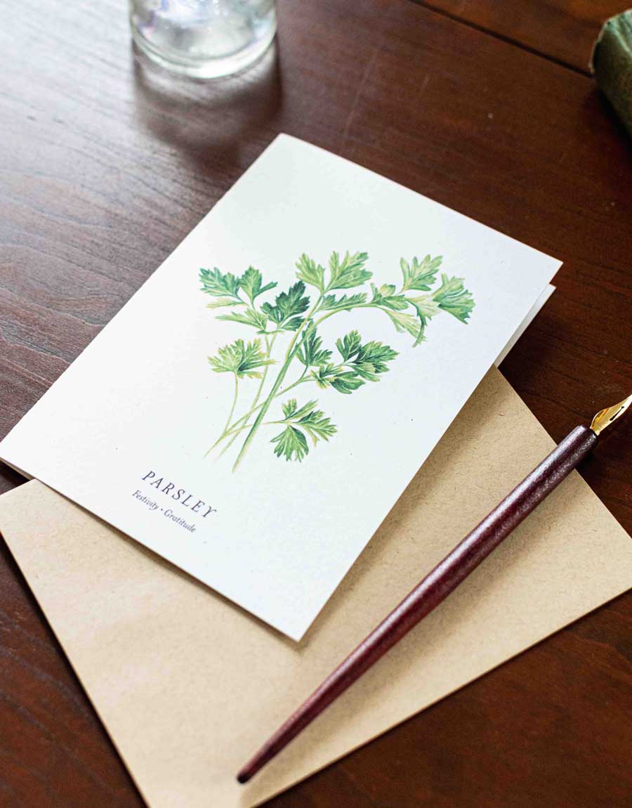 Note card with parsley illustration on a wooden desk with a pen