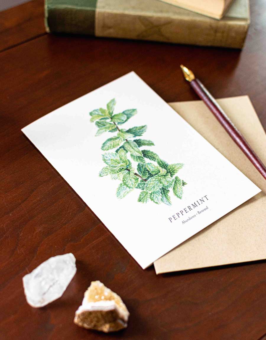 Note card with peppermint illustration on a wooden desk with a pen and rocks.