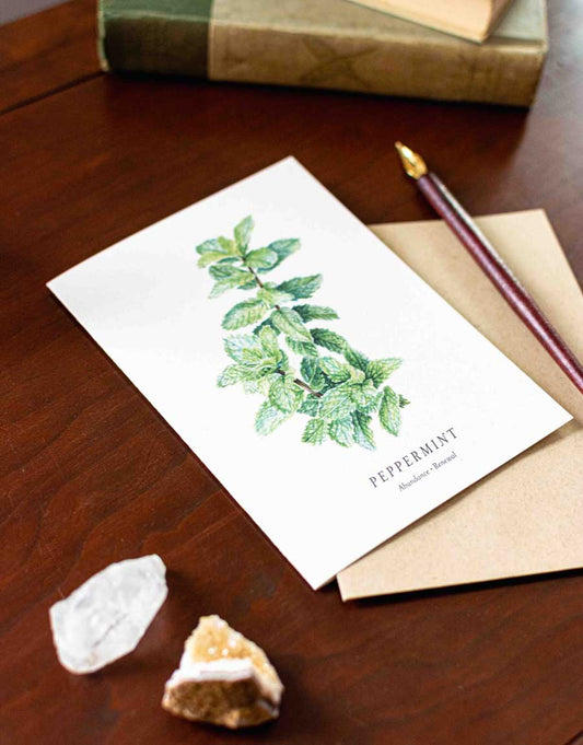 Note card with peppermint illustration on a wooden desk with a pen and rocks.