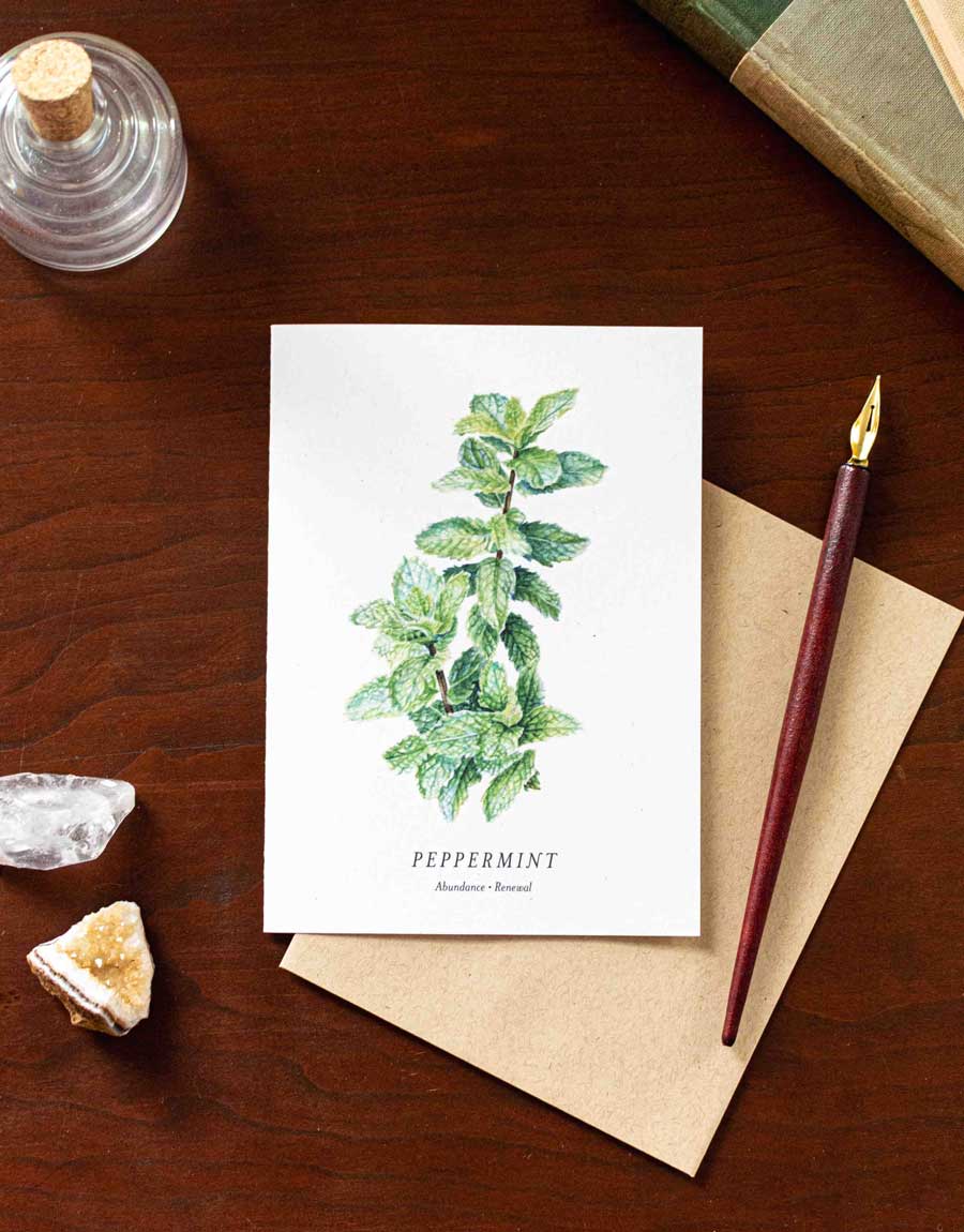 Greeting card with peppermint illustration on a wooden desk with a pen and crystals.