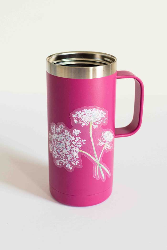 Pink travel mug with white floral sticker on a light background. 