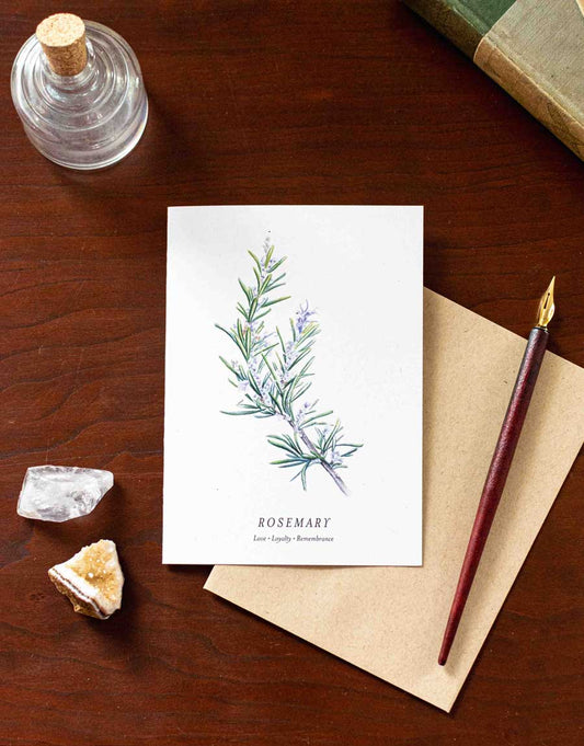 Greeting card with rosemary illustration on a wooden desk with a pen and crystals.