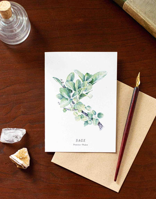 Note card with sage plant illustration on a wooden desk with pen and crystals
