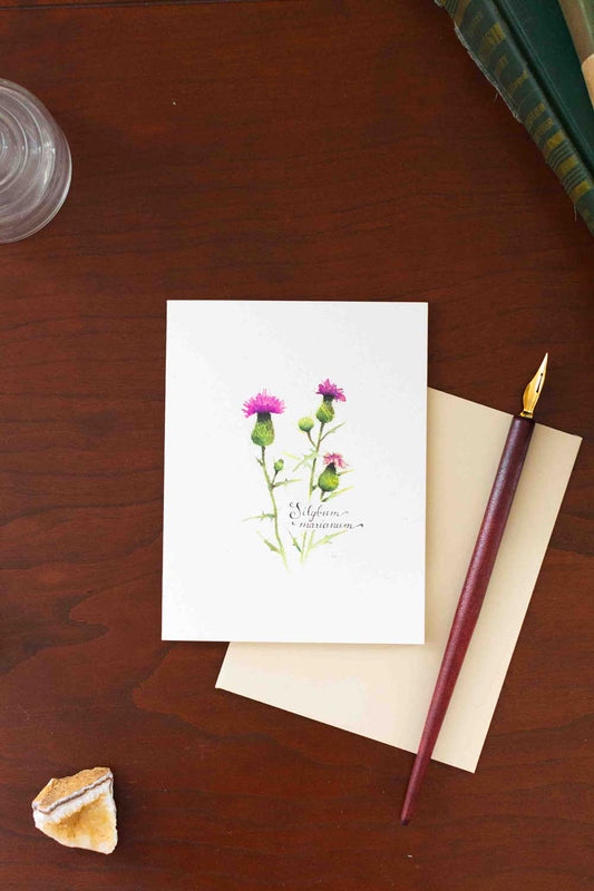 Greeting card with floral Thistle design on a wooden surface with a pen and paper.