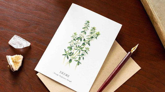 Note card with thyme plant illustration on a wooden desk with a pen and crystals.