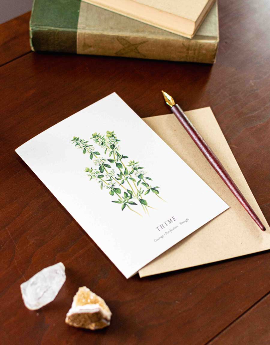 Note card with a thyme plant illustration, pen, and stones on a wooden desk