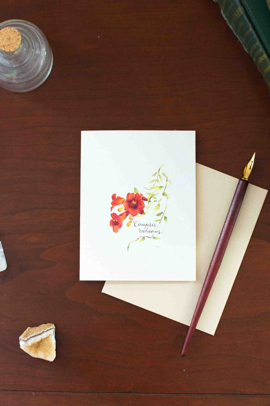 Greeting card with floral Trumpet Vine design on a wooden surface with a pen and small object.