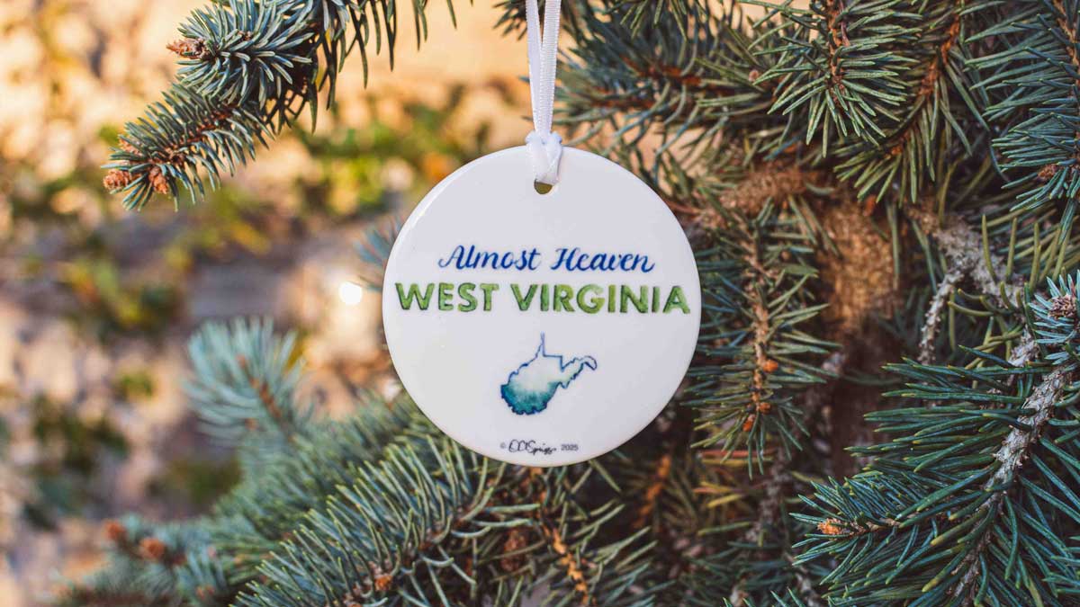Round ornament with 'Almost Heaven West Virginia' text hanging on a pine branch.