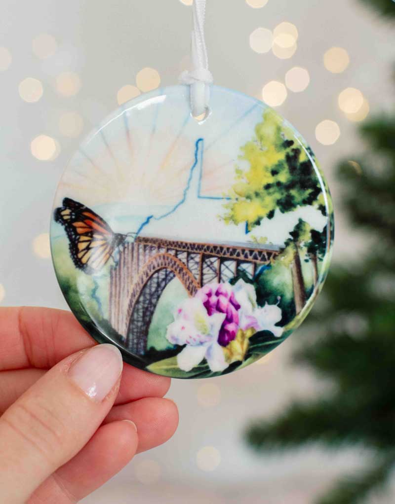 Decorative WV ornament with the New River Gorge bridge held by a hand against a blurred background.