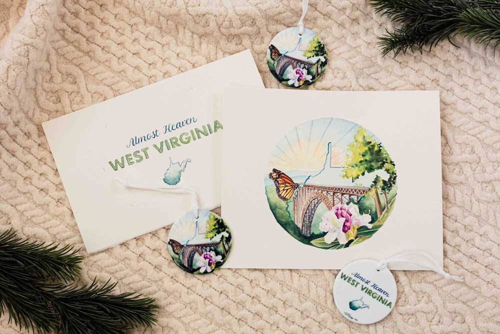 West Virginia-themed ornament and paintings on a textured surface with greenery.